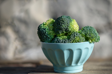 Healthy Green Organic Raw Broccoli Florets Ready for Cooking. Bunch of fresh green broccoli in bowl on wooden table close up on the background of a stone wall.の写真素材