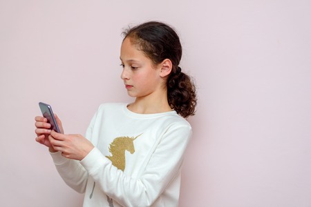 Beautiful young girl using modern smartpone, hipster child blogger typing text message on her cellphone.の写真素材