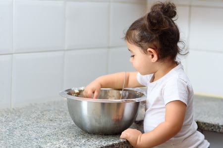Little kid girl making pancakes on marble table. Happy family funny child are preparing the dough, bake cookies in the white kitchen.の写真素材