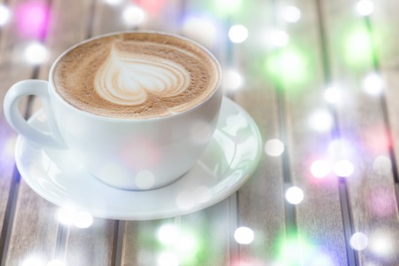 A cup of hot latte, cappuccino or espresso coffee with milk  foam on a  rustic table. White coffee mug with heart shape latte art on wood background. Copy space for text.の写真素材