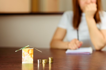 Middle age Woman With Model House from Israel Currencies new israeli shekel On wooden Table. Woman relaxing at home, building house from Israel 100 and 50 banknotes.Selective focus on money.の写真素材
