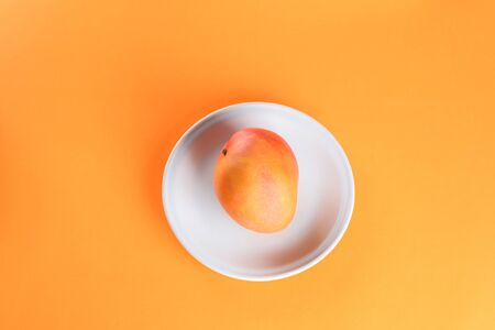 Fresh Mango tropical fruit on plate on orange background.Top view. Copy space. Mono-color, monochrome image.の写真素材