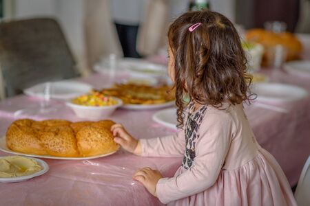 Little jewish curly girl placing challah bread on a table for Shabbat meal.