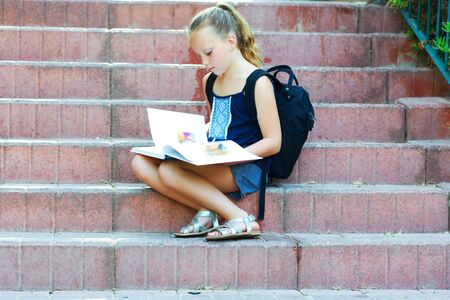 Happy smiling kid Back to school. Child little girl with bag go to elementary school. Child of primary school. Pupil go study with backpack. Schoolgirl 8 years old doing homework on stairs reads book.の写真素材