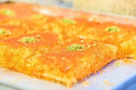 Sweet arab dessert kunefe, kunafa, kadayif with pistachio powder and cheese on the tray in the market.Selective focus.の写真素材