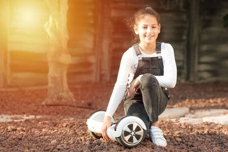 Beautiful kid Smile with Braces.Young hipster teenager girl sit with electric Hover Board, Dual Wheel Self Balancing Electric Skateboard at the sunny park, child using two-wheeled board. Copy space.の写真素材