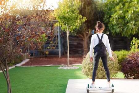 Back view of little girl riding a electric scooter outdoor. Young teenager balances on the...