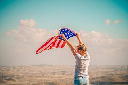 American flag. Back view little patriotic happy girl holding an american flag waving on blue sky background. National 4 july. Memorial day. Retro style.の写真素材