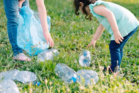 Kids cleaning in park.Close up hands volunteer child with a garbage bag cleaning up litter, putting plastic bottles in recycling bag.の写真素材
