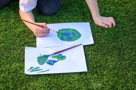 Close up kids hand drawnig a picture of earth globe.Child painting with brush and color a picture of earth.Earth day, plastic free and zero waste concept.の写真素材