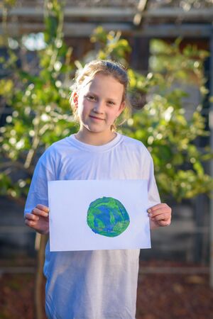 Portrait of the junior girl holding the drawing earth globe outdoor sunny day. Earth day, plastic free and zero waste concept.の写真素材
