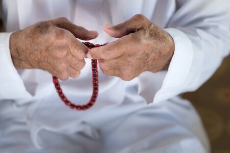 Arabic Bedouin Muslim man in traditional white holiday clothing.Praying hands of an old man holding rosary beadsの写真素材