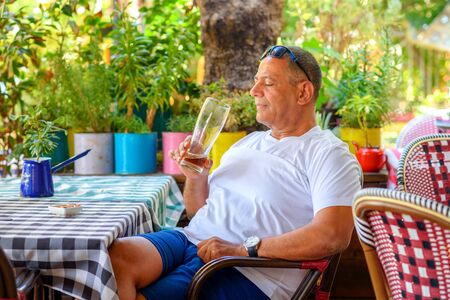 Middle Eastern man drinking beer. Side view of handsome middle aged man drinking beer while sitting at outdoor restaurant terrace.の写真素材