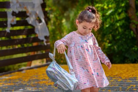 Curly cute little toddler girl back to school with holographic schoolbag or satchel, child going to...