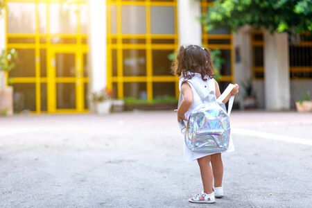 Back to school. Cute child girl with holographic backpack running and going to school with fun.Back, rear view of a toddler kid walking towards the preschool with the door in the background.の写真素材