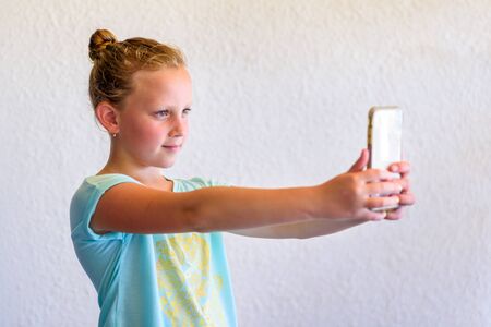 Portrait Of Stylish Girl In Neo Mint Color T-shirt Using Smartphone. Child Teenager Makes Vertical video Or Takes Photo For Story.の写真素材