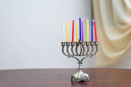 Jewish holiday Hanukkah background with menorah and colorful candles on wooden table in home. Cozy...
