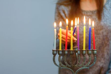 Jewish Woman lighting Hanukkah Candles in a menorah. People celebrate Chanukah by lighting candles on a menorah, also called a Hanukiyah. Each night, one more candle is lit.の写真素材