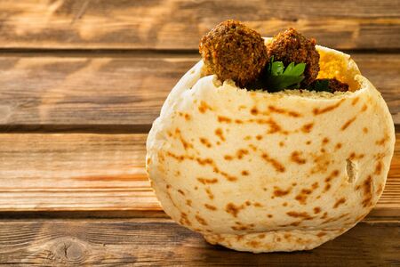 Falafel balls in a pita on a wooden background. Falafel is a traditional Middle Eastern food,commonly served in a pita great source of fiber, protein, copper, folate and other nutrients. Copy space.の写真素材