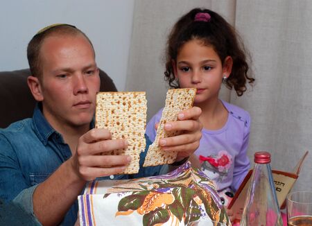 Jewish Family Celebrating Passover.Jewish man blessing on Matzah as they celebrate Seder. The feast is celebrated on the first night of Passover, holiday commemorating the Jews exodus from Egypt.の写真素材