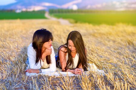 Two pretty brunette girls lying on gold cut wheat field and talking outdoor.Beautiful landscape.Travel concept.の写真素材