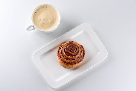 Perfect morning,sweet breakfast and start day.Coffee cup and Cinnamon Danish Swirl-classic buttery danish pastry rolled with cinnamon and glazed with sugar on dish on white background.の写真素材