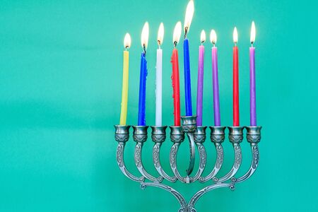 Jewish holiday Hanukkah background with menorah traditional candelabra and burning colorful candles.