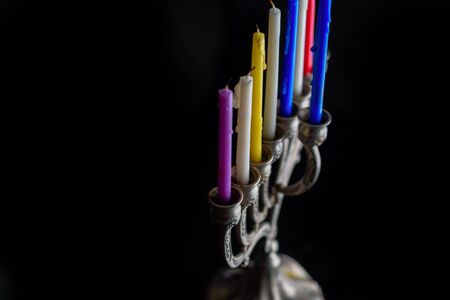 Menorah with many colorful candles on black background.