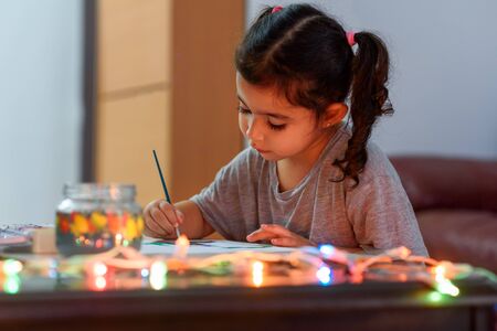 Portrait of cute little girl drawing at home with Christmas decorations. Real life, happy moments, cozy home.の写真素材