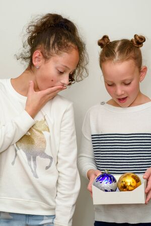 Two Surprised young teenage girl with hair bun over white background. Child holding baubles decoration for christmas tree.の写真素材