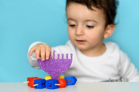 Jewish Boy Play With Festive Hanukkah Blue Purple Menorah And Colorful Wood Dreidels. Selective Focus.の写真素材
