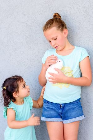 Teenager child holding a cute little white rabbit. Two happy young girls playing with bunny.の写真素材