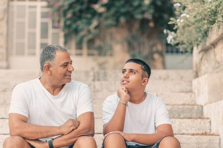 Teenager son and senior father sitting on stairs and talking. Two generation.の写真素材