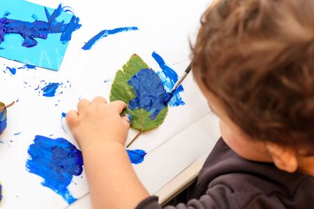 Little child painting leaves blue color, crafts and art therapy. Classic Leaf painting art. Child of stock contributor painting green leaves trendy blue color 2020.の写真素材