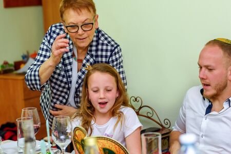 Jewish family celebrating Passover Seder reading the Haggadah. Three generations, real family.