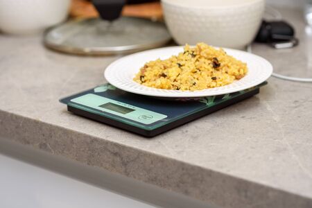 Bulgur, white fish and vegetables on a kitchen scale. Delicious healthy warm salad on a marble...