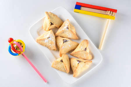 Purim holiday celebration. Hamantaschen cookies and wooden noisemaker or gragger on white...