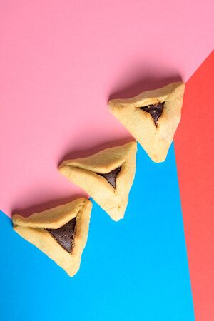 Purim holiday concept. Creative arrangement of Hamantash on red,pink and blue paper background. Hamantaschen triangular pastries also called Hamans pockets or Oznei Haman-Hamans ears.の写真素材