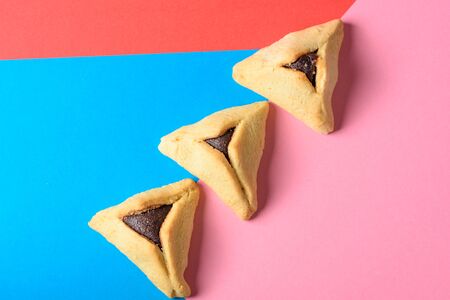 Purim holiday concept. Creative arrangement of variety Hamantash on red, pink and blue paper background. Hamantaschen triangular pastries also called Hamans pockets or Oznei Haman-Hamans ears.の写真素材
