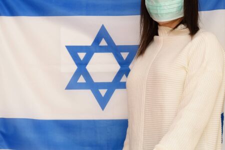 Israeli woman with medical face mask on Israel flag background. Israelis are in 14-day quarantine for coronavirus.の写真素材