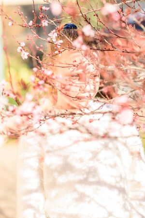 Young blonde girl surrounded by flowers of a springtime tree with beautiful shadows on her face and clothes.の写真素材