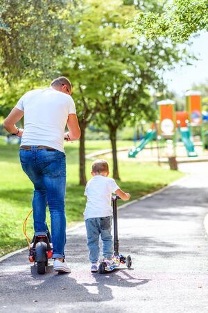 Faceless father On Electric Scooter With Her Son On Scooter Riding In Summer In City Park. Alternative Transportation.の写真素材
