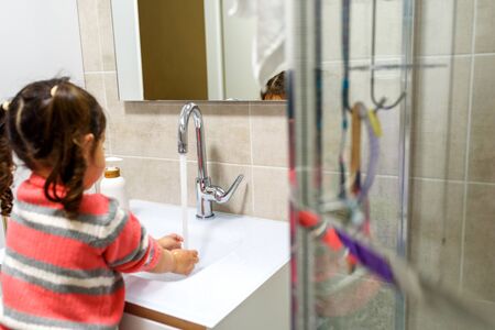 Toddler child washing her hands in the sink. Clean hands protect against infection and virus. Selective focus.の写真素材