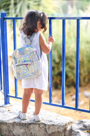 Child with bag back to school. Curly cute little girl back to school with holographic schoolbag....