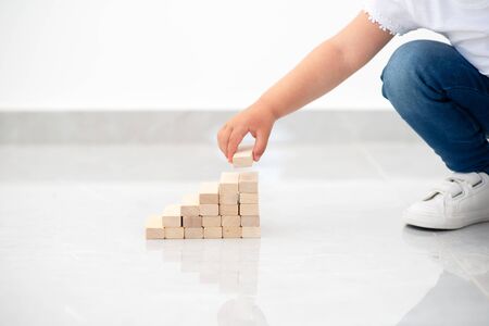 Close up child hand arranging wood block stacking as step stair. Instilling leadership skills in children, development, education. Ladder career path for business growth, early learning. Copy space.の写真素材