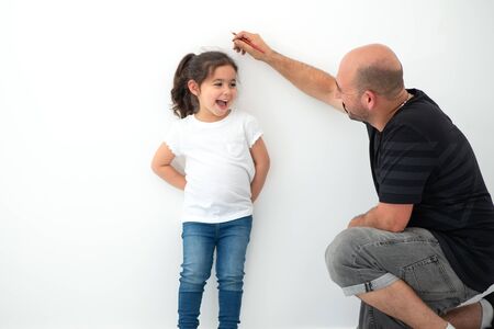 Father measuring height of a cute child. Dad measures the growth of her child daughter at a blank white wall.の写真素材