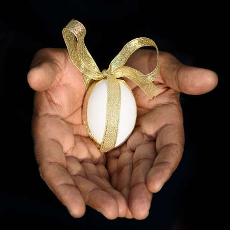 Close up of man hands holding a white egg with a gold ribbon. Safe delivery and insurance, proper...