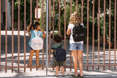 Happy diverse school children going to school outdoor at sunny day. Children near gate of closed school.の写真素材