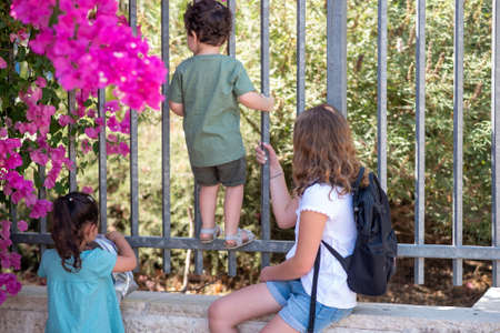 Little girls with blonde hair and black hair and toddler brother with curly hair look through a...