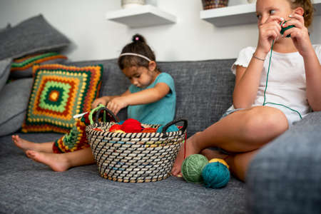 Children learning to knit, sitting on couch in the home. Girls knits crochet. Selective focus on...